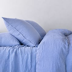 a bed with blue linens and pillows on top of it, in front of a white wall