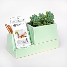 a cell phone sitting on top of a desk next to a green cup filled with succulents