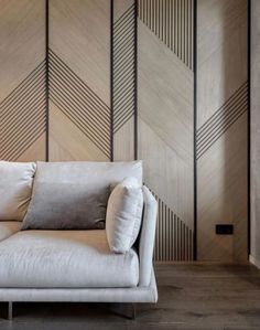 a white couch sitting in front of a wooden wall with geometric designs on it's walls