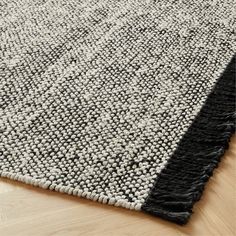 a black and white area rug with fringes on the bottom, in front of a wooden floor