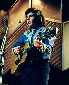 a man holding a guitar while standing in front of a microphone