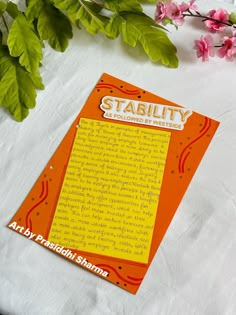 an orange and yellow book sitting on top of a white table cloth next to pink flowers