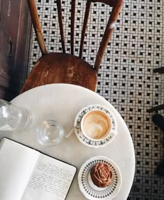 an open book and two cups of coffee on a white table with a wooden chair