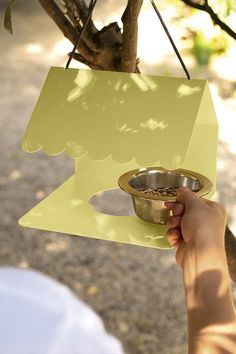 a person holding a metal bowl in front of a tree with a sign hanging from it