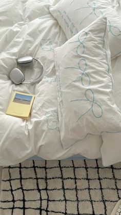 an unmade bed with white sheets and blue writing on the pillowcase, along with a pair of headphones