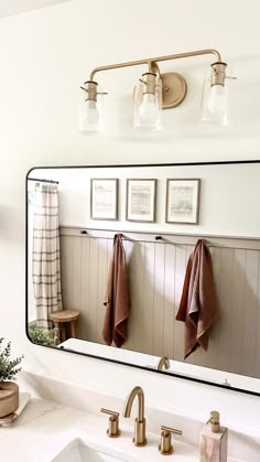 a bathroom mirror with three towels hanging on it's side and two lights above the sink