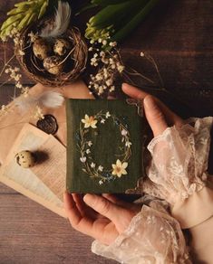 a person holding a small book with flowers on it, surrounded by other items and plants