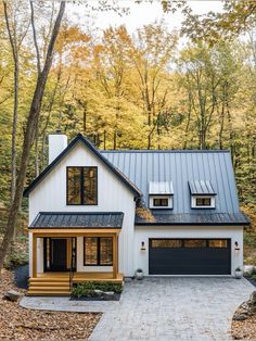 a white house in the woods with lots of trees and leaves on the ground around it