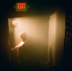 a person standing in front of a exit sign with light coming through the fog from behind