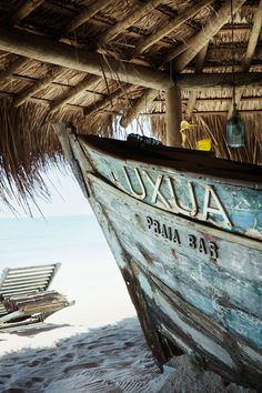 a boat sitting on top of a beach under a thatched roof next to the ocean