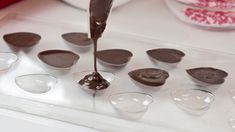 spoons filled with melted chocolate sitting on top of a white counter next to bowls