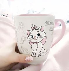 a woman's hand holding a coffee cup with a cartoon cat on the side