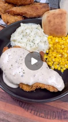 a black plate topped with fried chicken, mashed potatoes and gravy next to corn