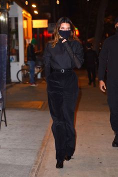 a woman walking down the street while wearing a black mask on her face and covering her mouth