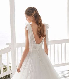 a woman in a white wedding dress standing on a porch with her back to the camera