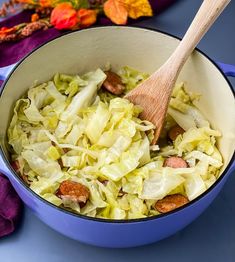 a blue pot filled with cabbage and sausage on top of a table next to a wooden spoon