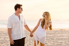 a man and woman holding hands on the beach