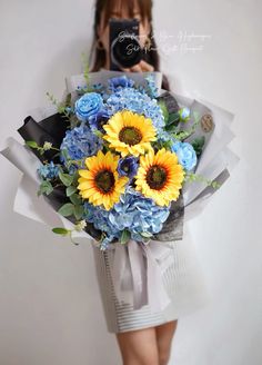 a woman holding a bouquet of blue and yellow flowers in front of her face while taking a selfie