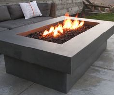 a fire pit sitting on top of a cement patio next to a couch and table