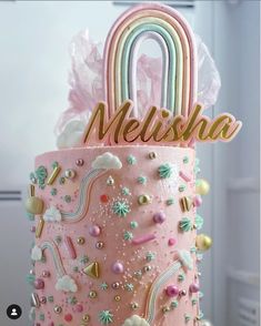 a pink cake decorated with rainbows, clouds, and a name on the top