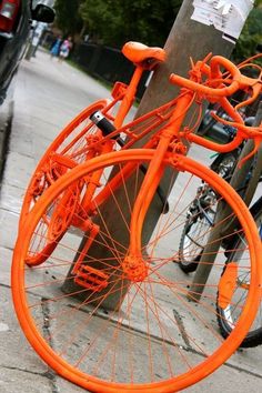 an orange bicycle parked next to a pole