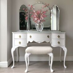 a white dressing table with mirror, stool and pink flowers in a vase on top