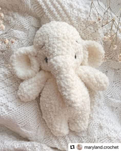 an elephant stuffed animal laying on top of a bed covered in white knitted blankets