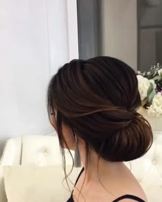 a woman sitting on a couch with her hair in a low bun and flowers behind her