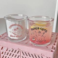 two glass candles sitting on top of a pink crate with the words super cute written on it