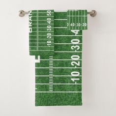 a green football field towel hanging from a metal hook on a white wall next to a pair of scissors