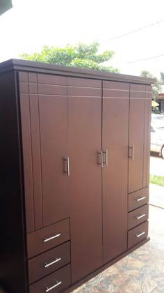 a large brown cabinet sitting on top of a tiled floor next to a tree and building