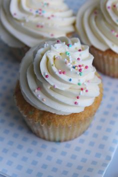 cupcakes with white frosting and sprinkles on a blue checkered tablecloth