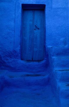 a blue building with steps leading up to it and a wooden door in the middle