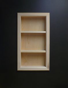 an empty wooden shelf on the wall next to a white toilet in a room with black walls