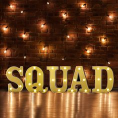 the word squad spelled out with lights in front of a brick wall and wooden floor