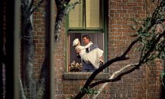 a man and woman kissing on the window sill in front of a brick building