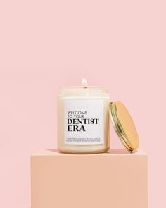 a white candle sitting on top of a pink block next to a jar of cream