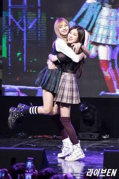 two girls are hugging on stage with their arms around each other and one girl is wearing a skirt