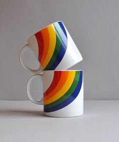 two white coffee mugs with multicolored stripes on them sitting side by side