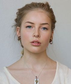 a woman in white shirt and necklace looking at the camera with serious look on her face