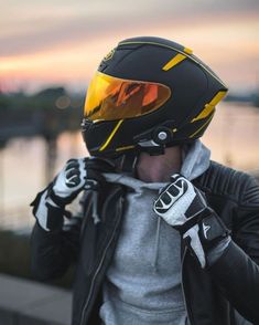 a man wearing a helmet and gloves while standing next to a body of water at sunset