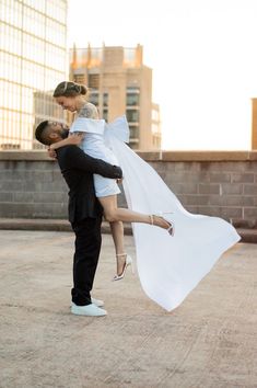 a man and woman are dancing in the middle of an empty lot with buildings in the background