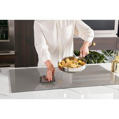 a woman is cooking food in a pan on the stove top, while she's wearing a white shirt