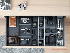 an open drawer with many different cameras and other things in it on top of carpeted flooring