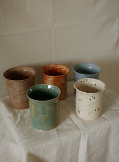 four different colored cups sitting on top of a white tablecloth covered table with a white cloth behind them