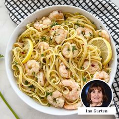 a white bowl filled with pasta and shrimp next to a lemon slice on top of a black and white checkered napkin