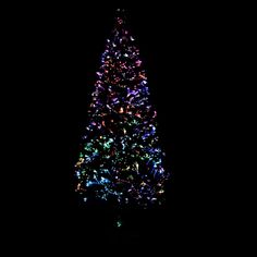 a large christmas tree is lit up in the dark with colorful lights on it's sides