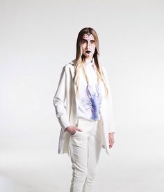 a woman with makeup on her face standing in white pants and a blazer jacket