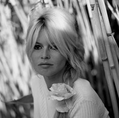 a woman with long blonde hair wearing a white sweater and flower in front of bamboo stalks