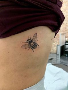 a woman with a bee tattoo on her lower back side ribcage, showing it's black outline